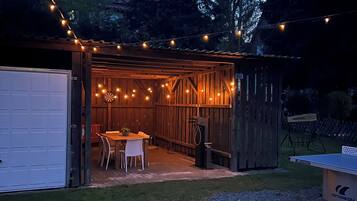Ein Holzschuppen mit Tisch und Stühlen, umgeben von einer Lichterkette.