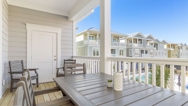 A wooden deck with a table and chairs, a white door, and a view of multi-story buildings in the background. - A FEW STEPS TO OCEAN in EMERALD ISLE, NC! Come visit walk to all entertainment! (Emerald Isle)