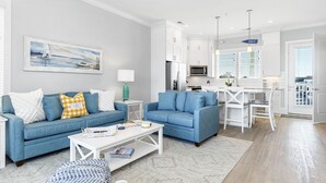 A modern living room with two blue sofas, a white coffee table, and a painting of a sailboat. - A FEW STEPS TO OCEAN in EMERALD ISLE, NC! Come visit walk to all entertainment! (Emerald Isle)
