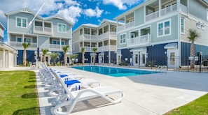 A multi-story residential building with a swimming pool, lounge chairs, and a well-maintained lawn.