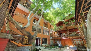 Ein Innenhof mit Holzhäusern, einem zentralen Baum und einem gepflasterten Weg.