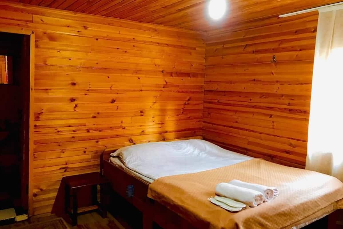 A wooden cabin room with a bed, a bench, and a ceiling light.