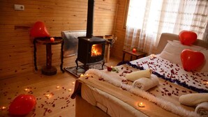 Ein gemütliches Zimmer mit Kaminofen, einem Bett mit Rosenblättern und herzförmigen Ballons, sowie einer Holzvertäfelung.
