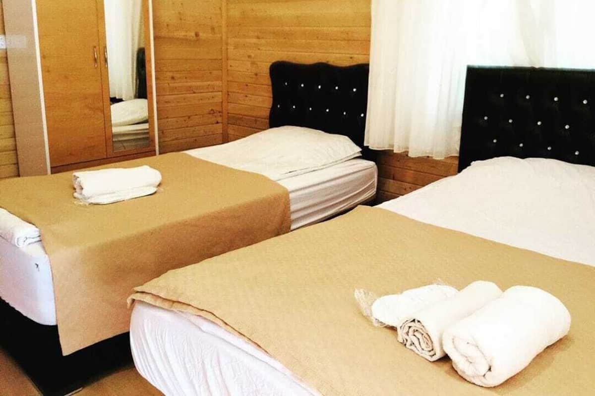 Two single beds with beige linens, a wooden wardrobe, and a mirror.