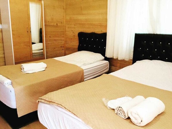 Dos camas individuales con ropa de cama color beige, un armario de madera y un espejo.