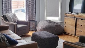 A living room with a sofa, ottoman, and a TV on a wooden cabinet. - Historic 1895 Queen Anne Victorian that is 131 years young (Lead)