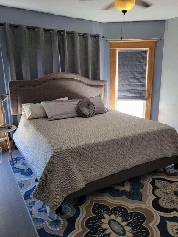 A bedroom with a large bed, a ceiling fan, and a window with curtains.
