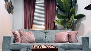 Een grijze bank met roze kussens, een houten doos met brieven en een afstandsbediening op een ronde tafel.