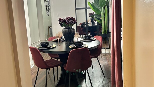 Een eethoek met een ronde tafel, rode stoelen en een grote potplant.