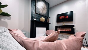 Een moderne woonkamer met een open haard, een tv met het Netflix logo en een gezellig zithoekje met zachte fauteuils.