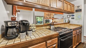 Une cuisine avec des meubles de rangement en bois, une machine à café, une bouilloire et une cuisinière.