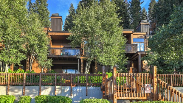 Un immeuble à plusieurs étages doté de balcons, entouré d’arbres et d’une clôture en bois.