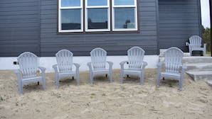 En bygning med en grå facade og fire Adirondack-stole stillet op foran.