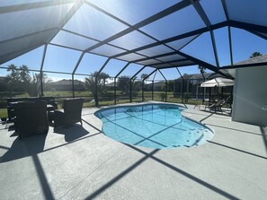 A covered outdoor swimming pool with a clear view of the surrounding landscape, including a lawn and distant buildings.