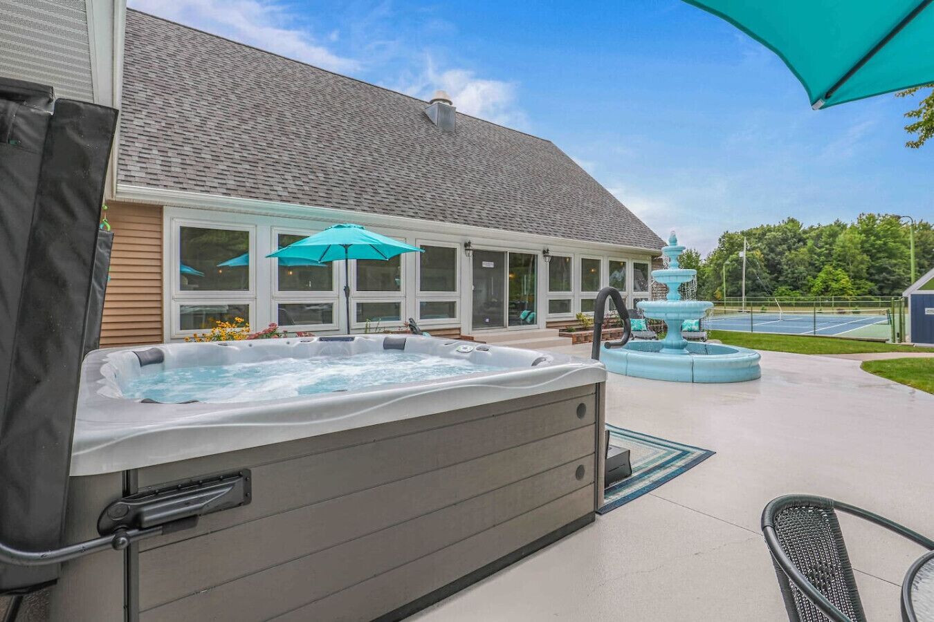An outdoor hot tub area with a covered seating area, a fountain, and a tennis court in the background.