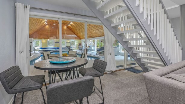 Un interior moderno con zona de piscina, escalera y mesa de comedor con sillas.