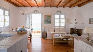 A spacious living room with wooden beams, a dining area with a table and chairs, and a kitchen with a tiled backsplash. - Tinos Agios Sostis Villa Filippos  five (5) min  walk to the beach - Pet Allowed (Agios Sostis Tinos)