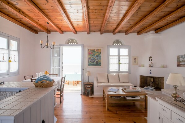 A spacious living room with wooden beams, a dining area with a table and chairs, and a kitchen with a tiled backsplash.