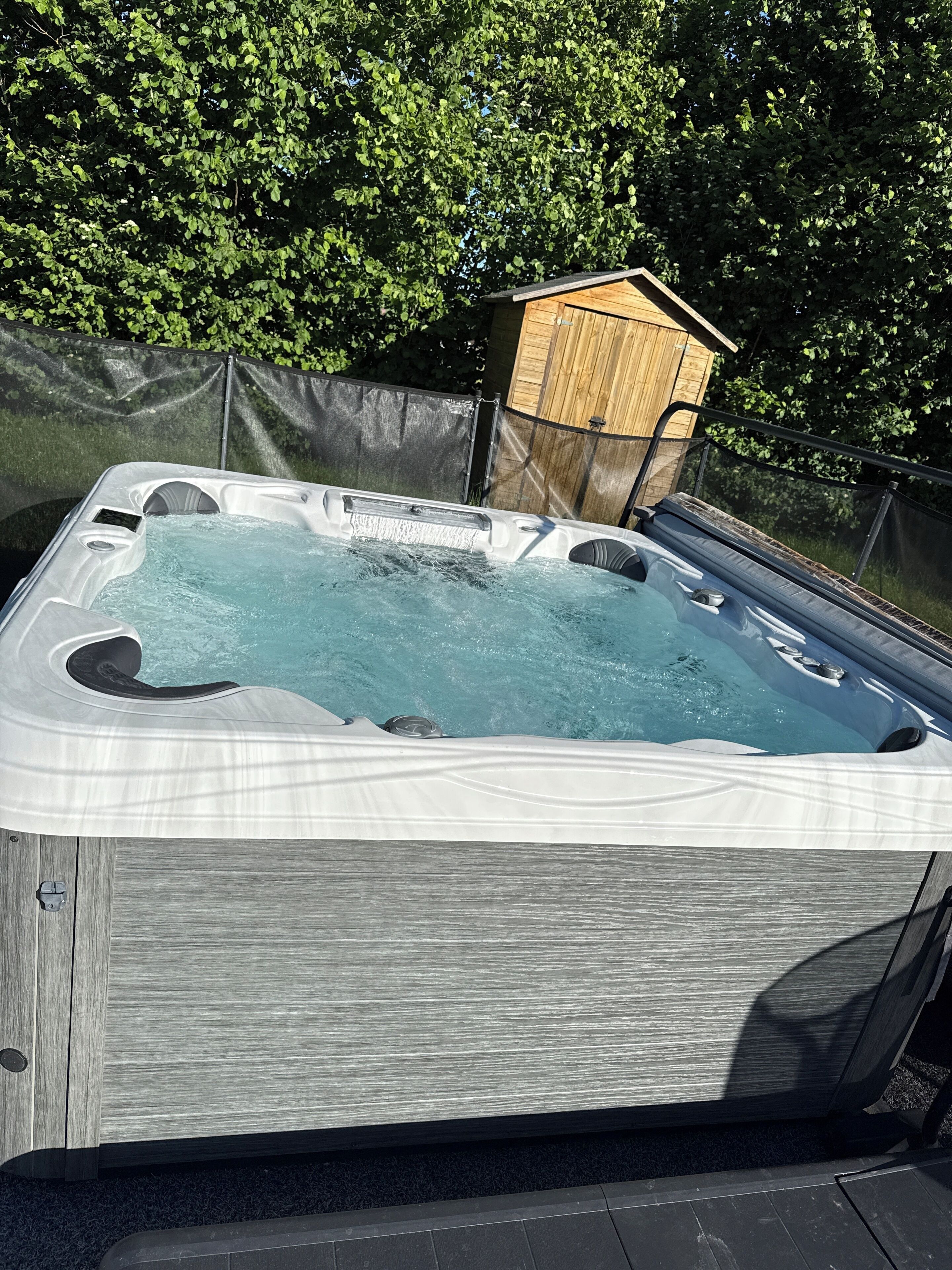 A hot tub with a wooden deck and a wooden structure in the background.