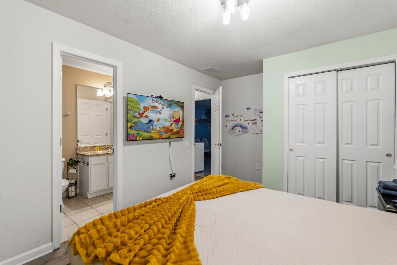 A bedroom with a bed, a painting, a door, and a bathroom visible through an open door.