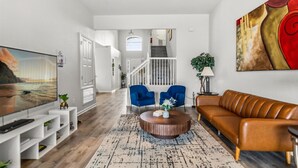 Un salon moderne avec un téléviseur à écran plat, un canapé en cuir marron, deux fauteuils bleus et une table basse.