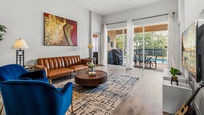 Un salon spacieux avec un canapé en cuir marron, des fauteuils bleus, une table basse et un grand tableau accroché au mur.