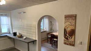 Keittiössä on laatoitettu seinäosa työtason yläpuolella, työtasolla on leivänpaahdin ja kori, ja ruokailutilassa on pöytä ja tuolit.