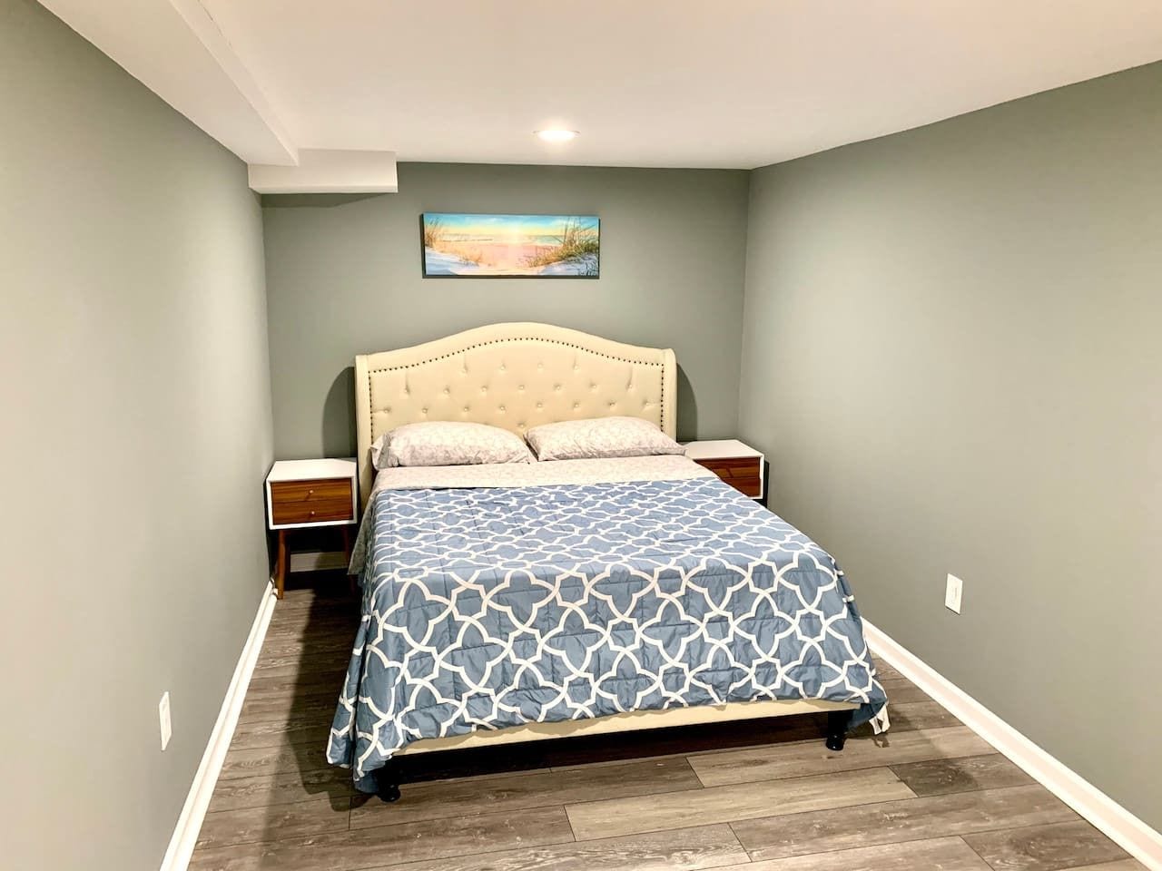 A bedroom with a bed, nightstands, a painting on the wall, and a wooden floor.