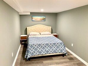 Un dormitorio con cama, mesitas de noche, un cuadro en la pared y suelo de madera.