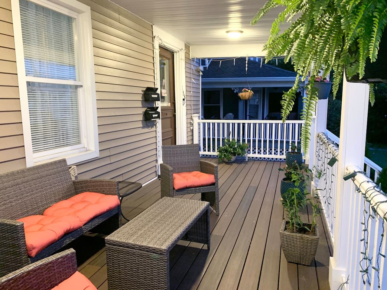 A covered outdoor deck with wicker furniture, potted plants, and a white railing.