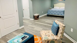 Une chambre à coucher avec un lit, une chaise, une petite table sur laquelle se trouve un livre et un tableau accroché au mur.