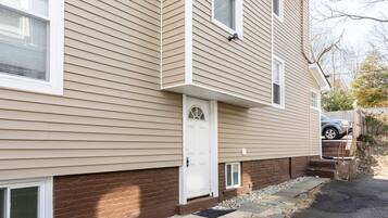 A two-story residential building with a beige siding exterior, a white front door, and a small front porch.