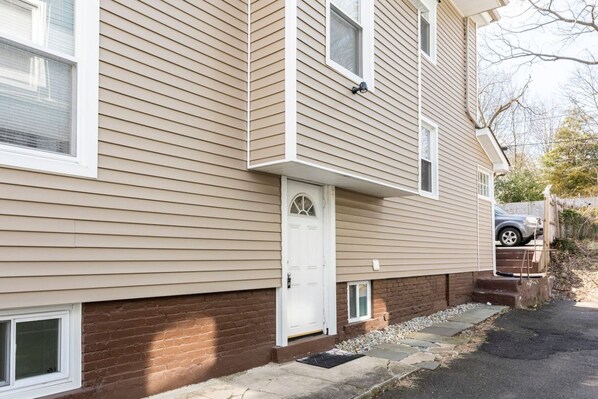 A two-story residential building with a beige siding exterior, a white front door, and a small front porch. - Semi Private cozy studio near downtown. (Montclair)