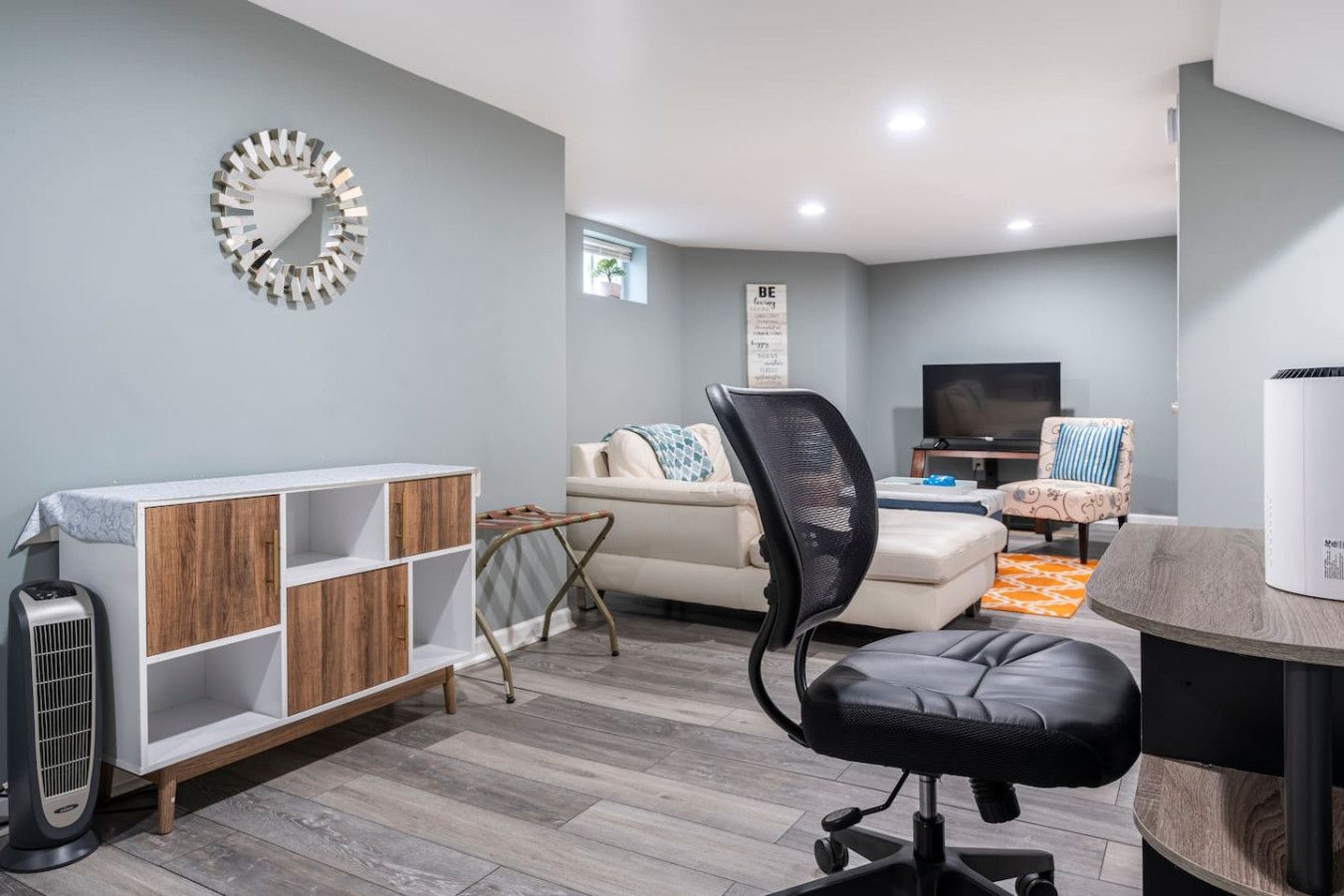 A modern living room with a sofa, a black office chair, a wooden cabinet, and a TV.