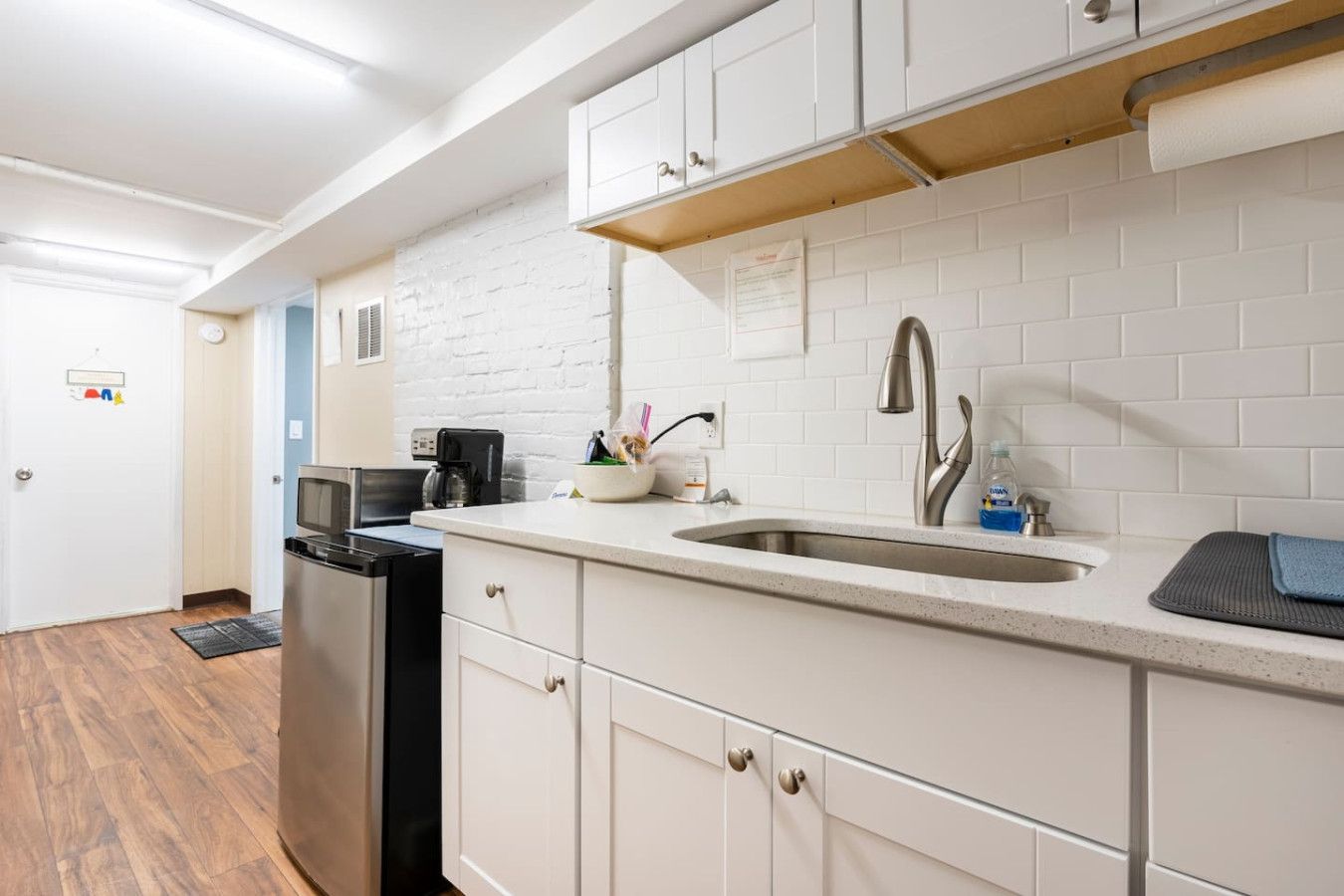 A modern kitchen with white cabinetry, a stainless steel sink, and a coffee maker.