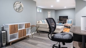 Un salon moderne avec un canapé, un fauteuil de bureau noir, un meuble en bois et un téléviseur.