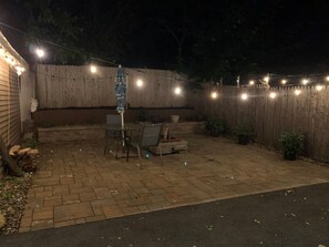 A backyard patio with a brick floor, a table and chairs, and string lights. - Semi Private cozy studio near downtown. (Montclair)