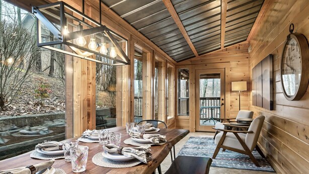 Un intérieur en bois avec une table à manger dressée pour quatre personnes, de grandes fenêtres et une horloge au mur.