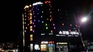 Et hotel med flere etager og oplyst skiltning, herunder et tydeligt 'HOTEL' skilt og et 'PARKERING' skilt.