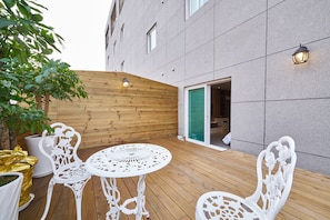 Un patio al aire libre con terraza de madera, sillas de hierro forjado blanco y una mesa redonda.