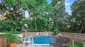 A wooden deck with a swimming pool, surrounded by trees and a wooden fence.