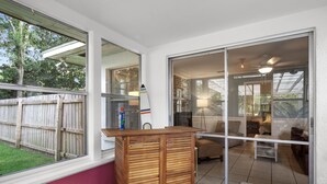 A room with a sliding glass door leading to a patio, a wooden desk, and a surfboard leaning against the wall.