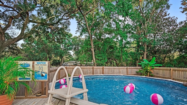 A backyard with a wooden deck, a swimming pool, and a safety sign.