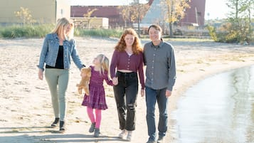 Eine Familie geht auf einem sandigen Pfad neben einem Gewässer, im Hintergrund sind Industriegebäude zu sehen.