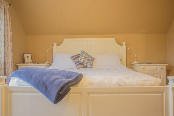 A neatly made bed with a patterned pillow, a folded blanket, and a bedside table with a lamp.