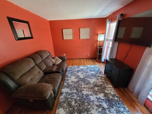 A living room with a brown sofa, a patterned rug, and a flat-screen TV on a stand. - Newly available Masters week rental (Evans)