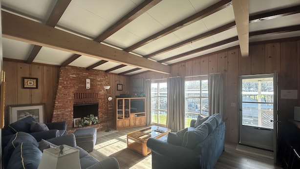 A cozy living room with a fireplace, wooden beams, and large windows. - Cozy 2 Bed 2 Bath Lake Front Cottage (Afton)