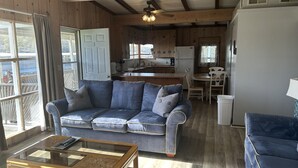 A cozy living room with a blue sofa, a glass-top coffee table, and wooden beams on the ceiling. - Cozy 2 Bed 2 Bath Lake Front Cottage (Afton)