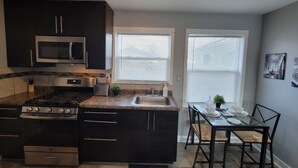 A modern kitchen with dark cabinetry, a built-in microwave, a gas stove, and a small dining area with a table and chairs. - Newly remodeled 1 Bedroom apartment (Ypsilanti)