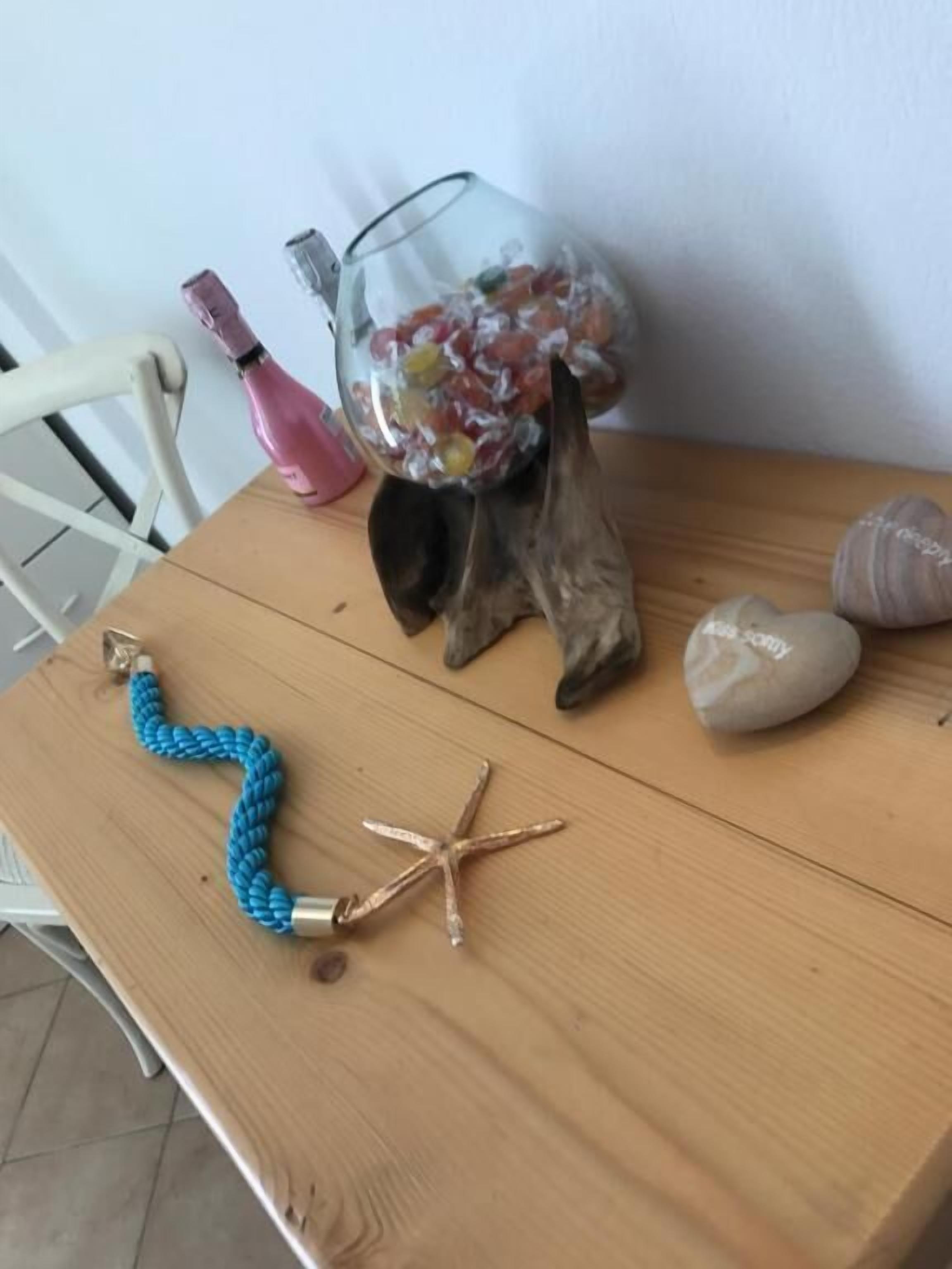A wooden table with a glass vase containing colorful candies, a blue rope, a starfish, and two heart-shaped rocks.